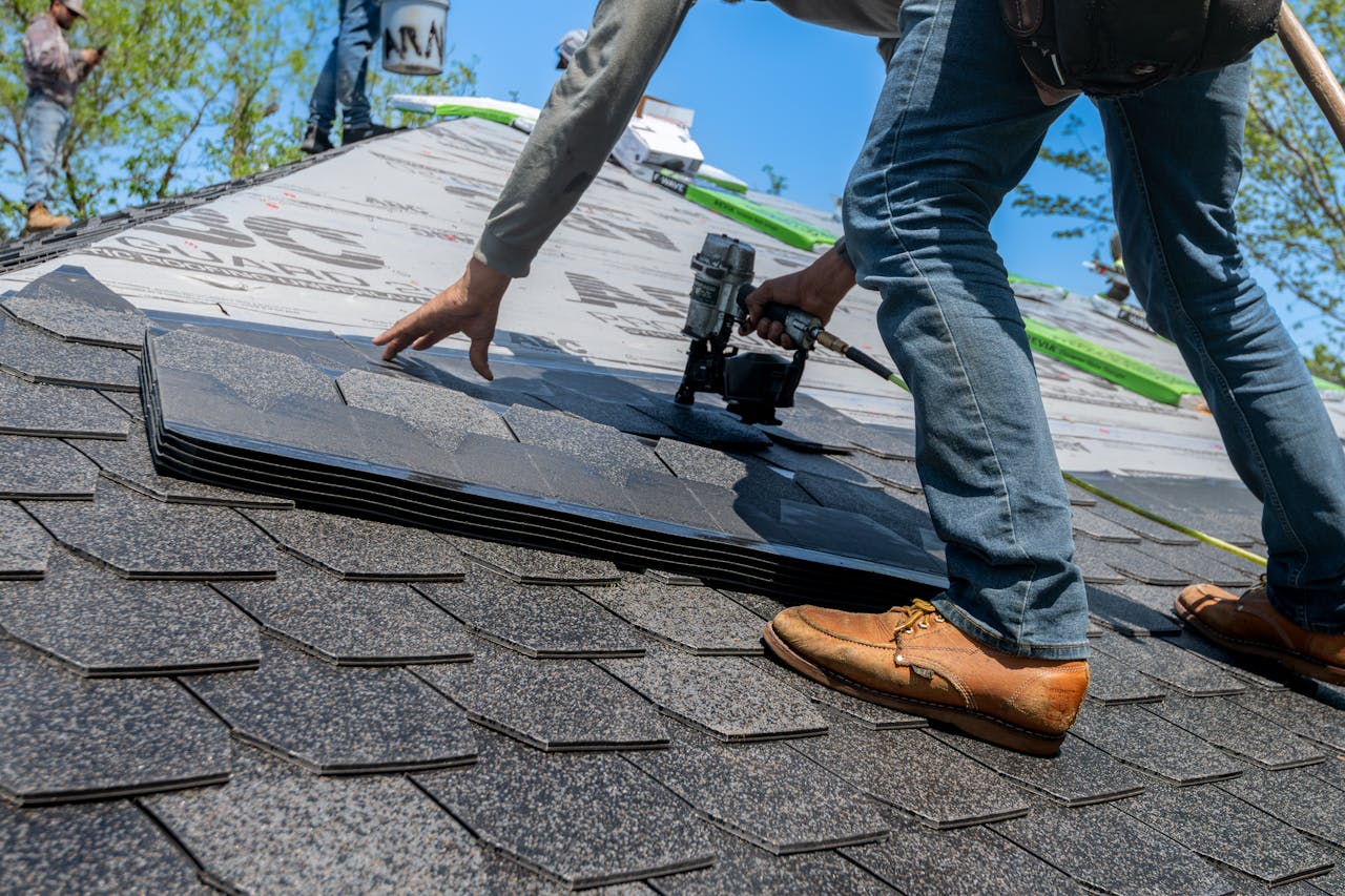 services-10 Roofer using nail gun for shingle installation on residential roof.