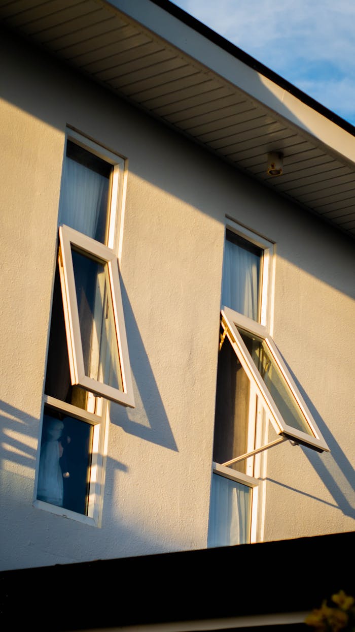 services-07 Close-up view of a white building with open windows at sunset, highlighting architectural details.